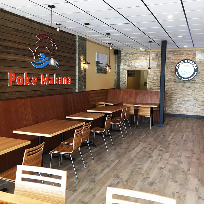 Bright dining area with large live-edge wooden table, glass pendant lights, and coastal artwork at Poke Makana, a Hawaiian restaurant in Sherwood