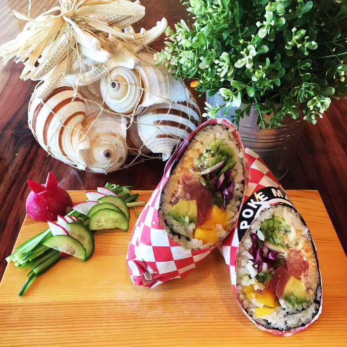 Two poke burritos wrapped in checkered paper, served with fresh veggie garnish and coastal decor at Poke Makana, a Hawaiian restaurant in Sherwood